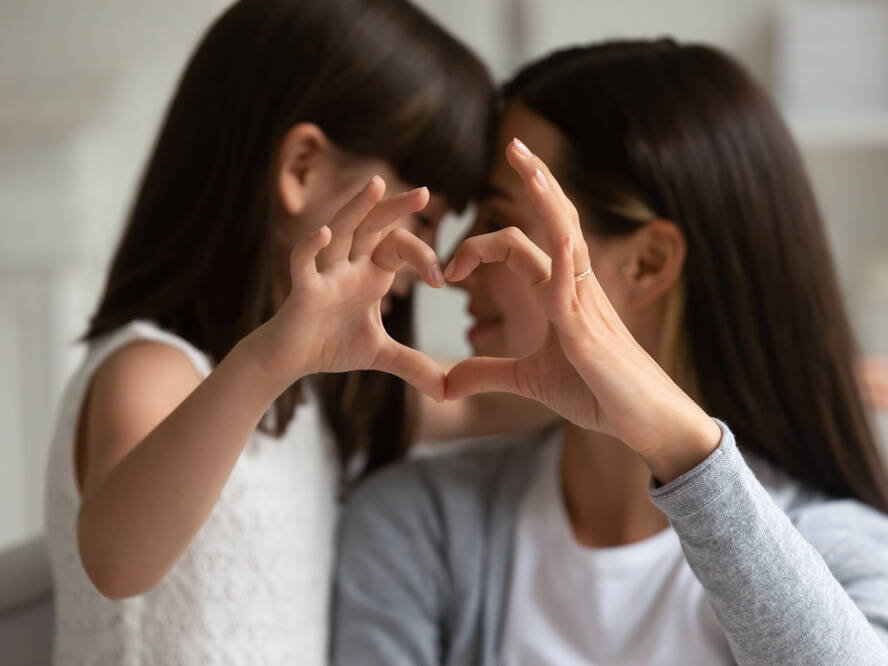 Mother and young daughter connect hand and form a heart