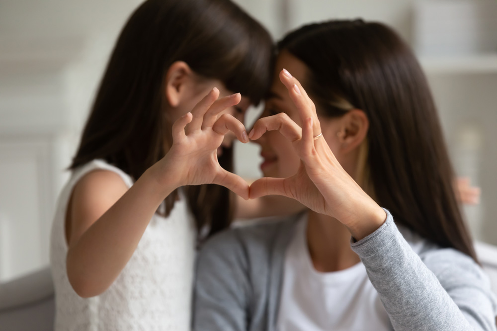 Mother and young daughter connect hand and form a heart