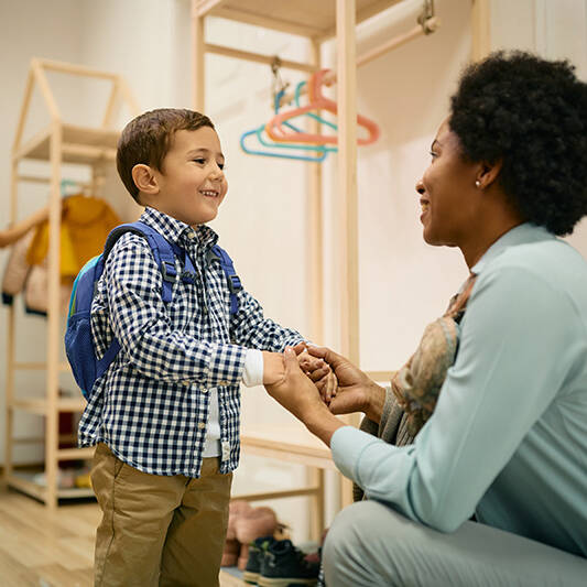 Happy little boy holding hands with his teacher on first day of preschool