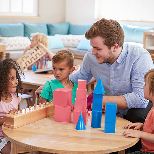 Male educator playing with preschoolers at the table