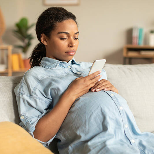 pregnant woman using smartphone sitting on couch at home