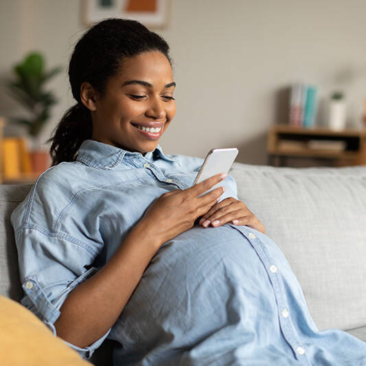 Pregnant Woman Smiling Using Mobile Phone Texting Sitting At Home