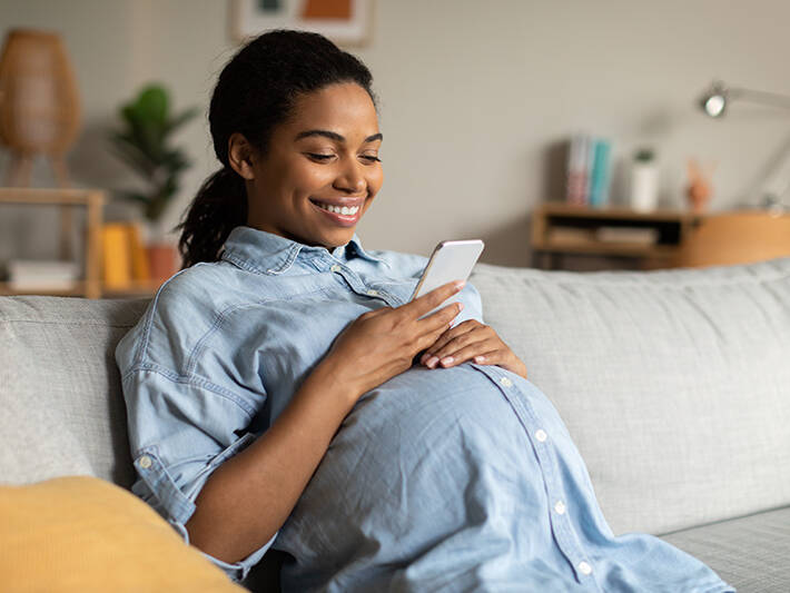 Pregnant Woman Smiling Using Mobile Phone Texting Sitting At Home