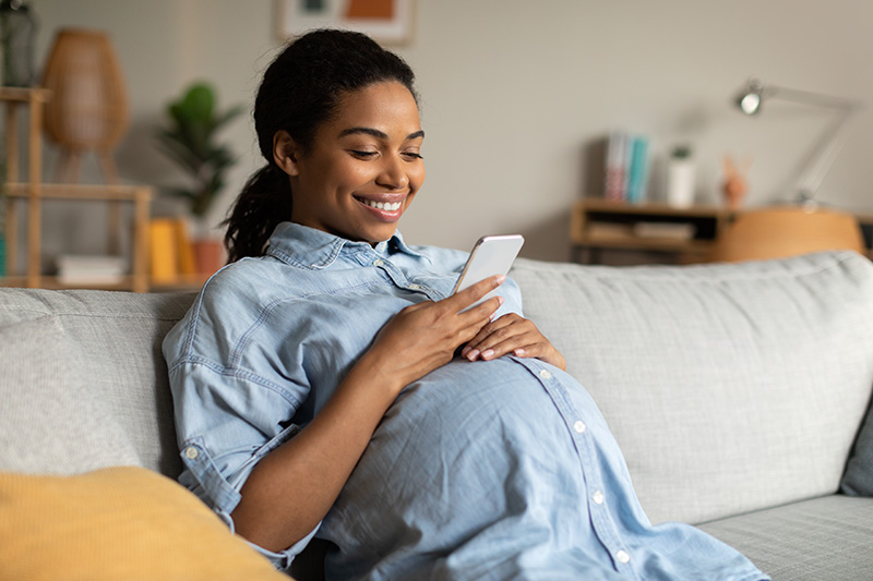 Pregnant Woman Smiling Using Mobile Phone Texting Sitting At Home