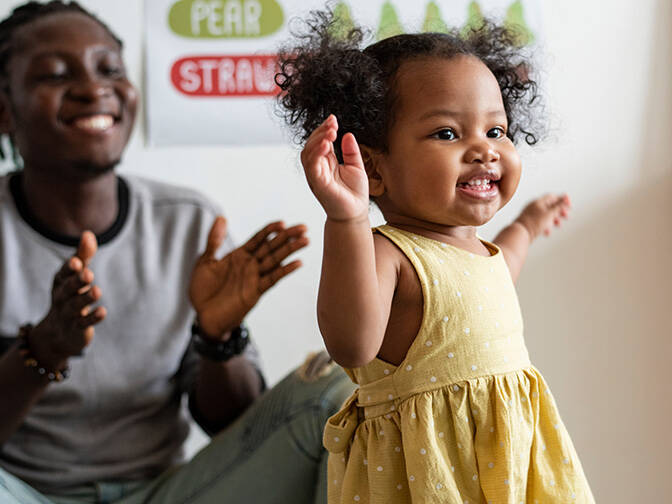 father clapping at toddler walking