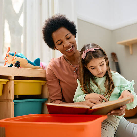 female teacher and little girl read book at kindergarten